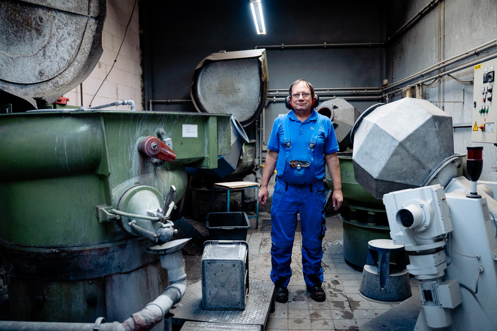 a man in a blue overalls and headphones standing in a room with large machines